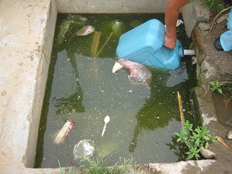 Eine Bewohnerin fllt den Bidon mit
                        frischem Wasser, und der Bidon selbst ist im
                        total verschmutzten Wasser, Nahaufnahme